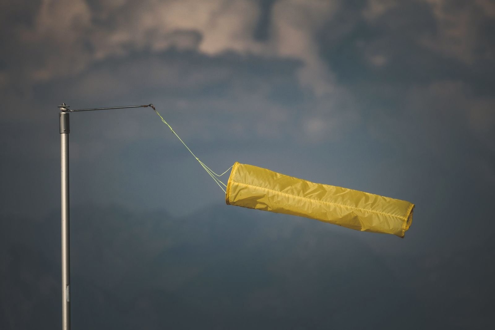 A yellow windsock standing out in a gusty wind against a dark storm sky